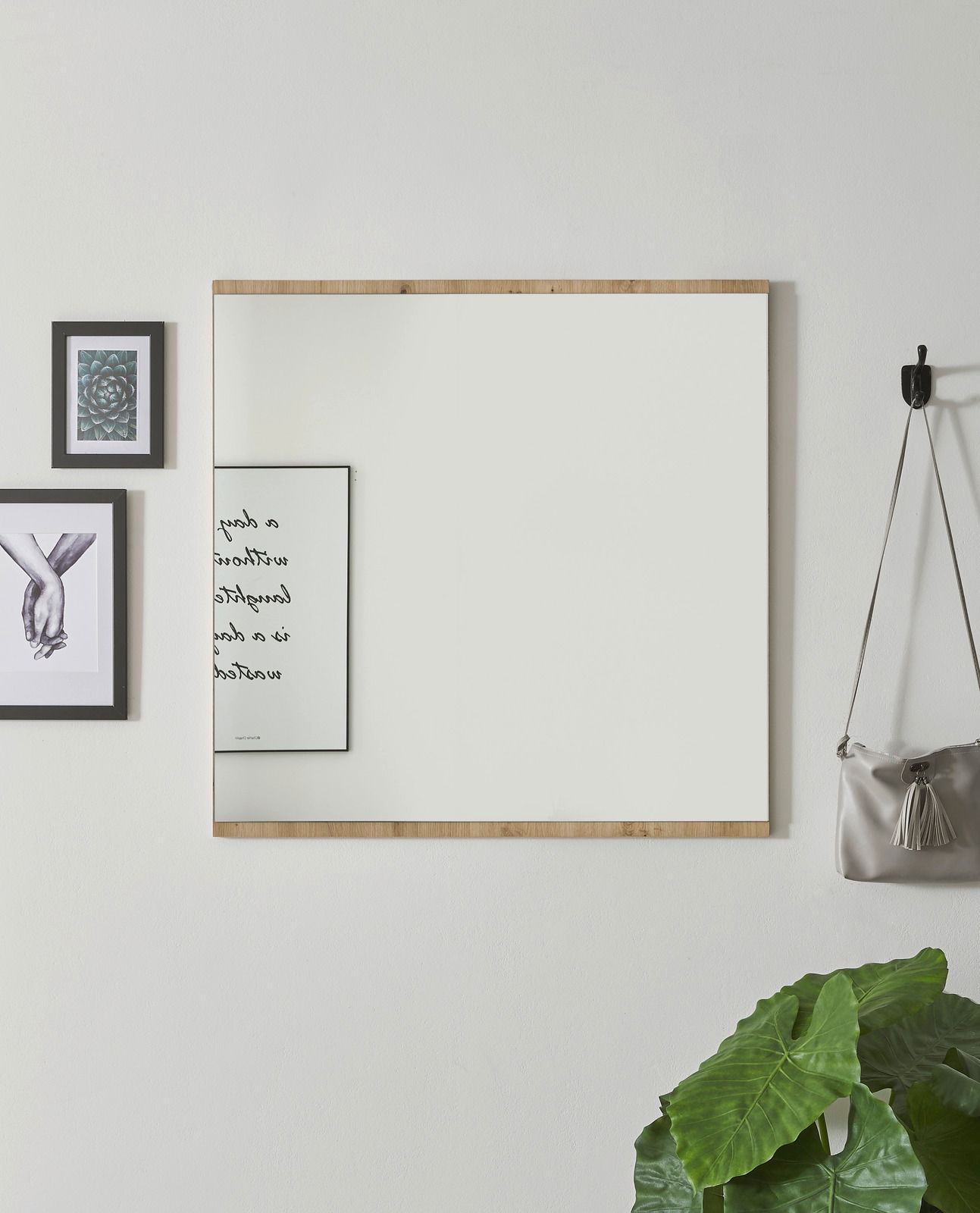 Moderner Wandspiegel mit Holzrahmen, frontal fotografiert, umgeben von Dekorationen wie Bildern und einer Pflanze.