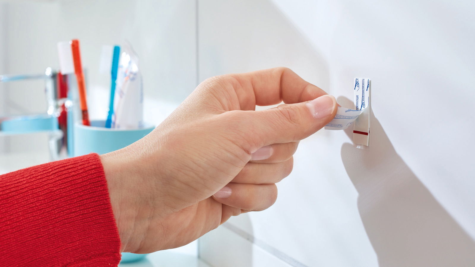 Hand befestigt einen tesa Powerstrip Haken Small an einer Wand im Badezimmer, seitliche Perspektive.