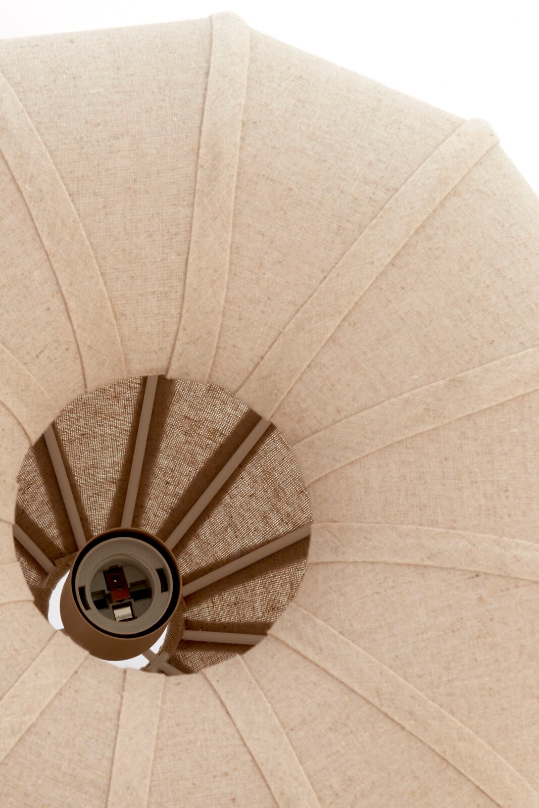 Nahaufnahme einer Hängeleuchte von unten, die einen textilen Lampenschirm in Beige zeigt.