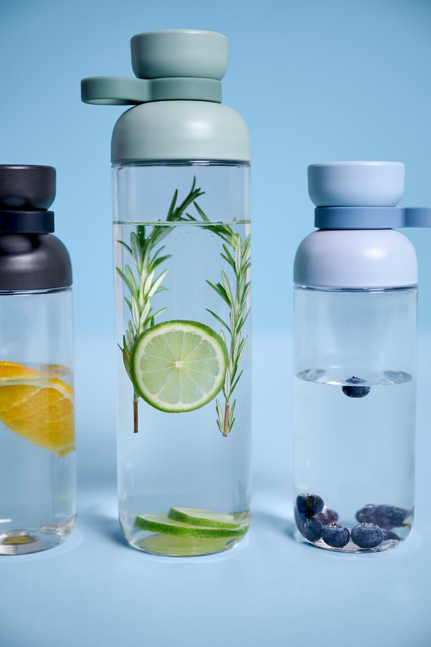 Mepal Trinkflasche Nordic Blue VITA Drei Trinkflaschen mit farbigen Deckeln, gefüllt mit Wasser und verschiedenen Früchten, aus der Frontalperspektive fotografiert.