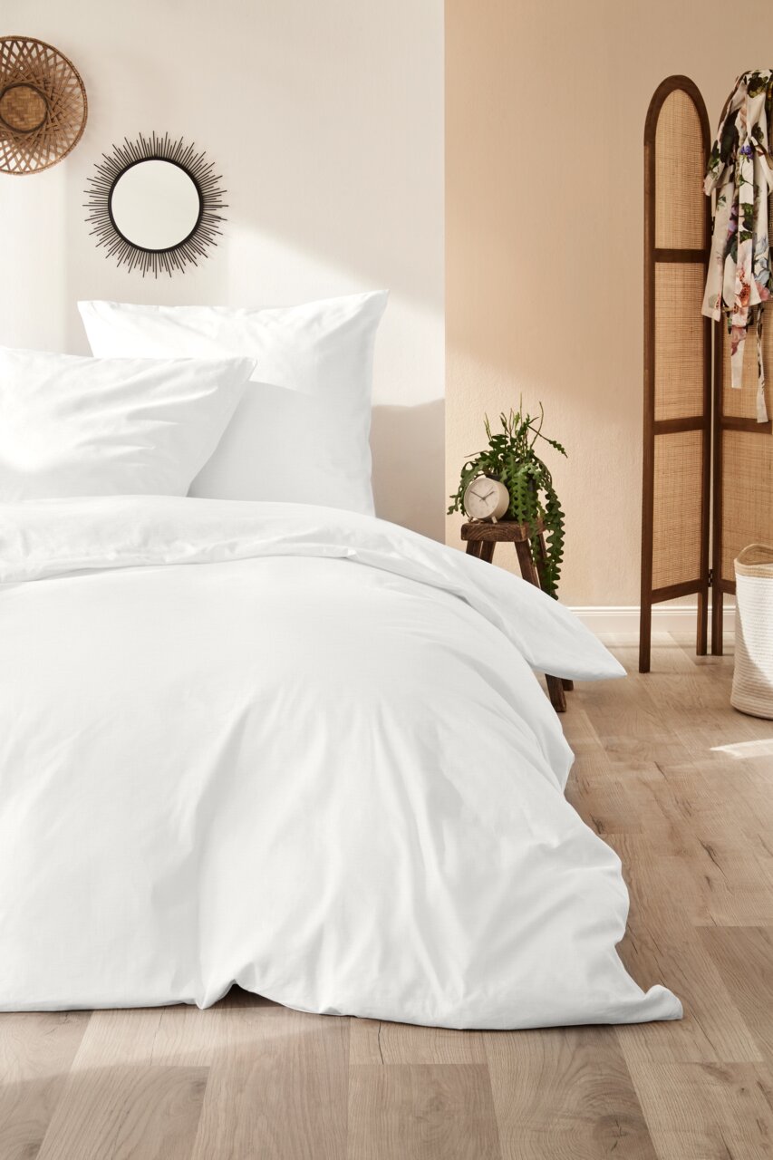 Weiße Bettwäsche auf einem Bett in einem gemütlichen Schlafzimmer, seitliche Perspektive.