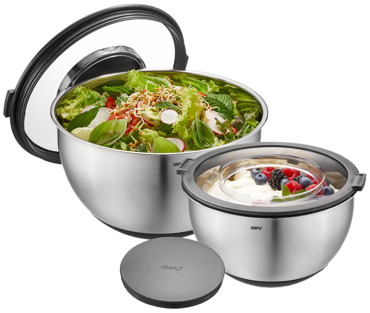 GEFU Schüssel-Set mit Spritzschutzd MUOVO Zwei Edelstahl-Schüsseln mit Spritzschutzdeckel, gefüllt mit Salat und Dessert, aus seitlicher Perspektive.
