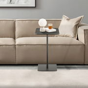Moderner Beistelltisch in schwarzem Design, frontal vor einem beigen Sofa platziert, mit einer Lampe und einem Glas auf der Tischplatte.