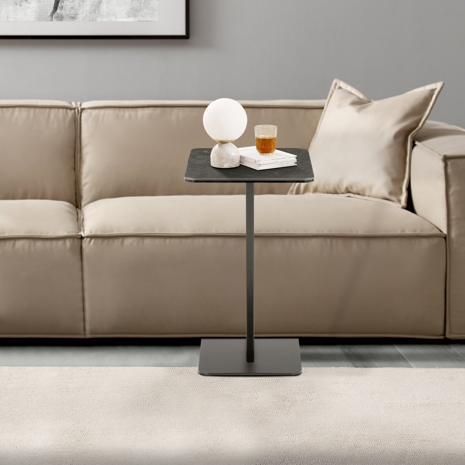 Moderner Beistelltisch in schwarzem Design, frontal vor einem beigen Sofa platziert, mit einer Lampe und einem Glas auf der Tischplatte.