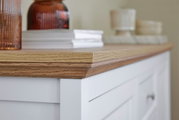 Nahaufnahme eines weißen Sideboards mit Holzplatte, dekoriert mit Büchern und Vasen, seitliche Perspektive