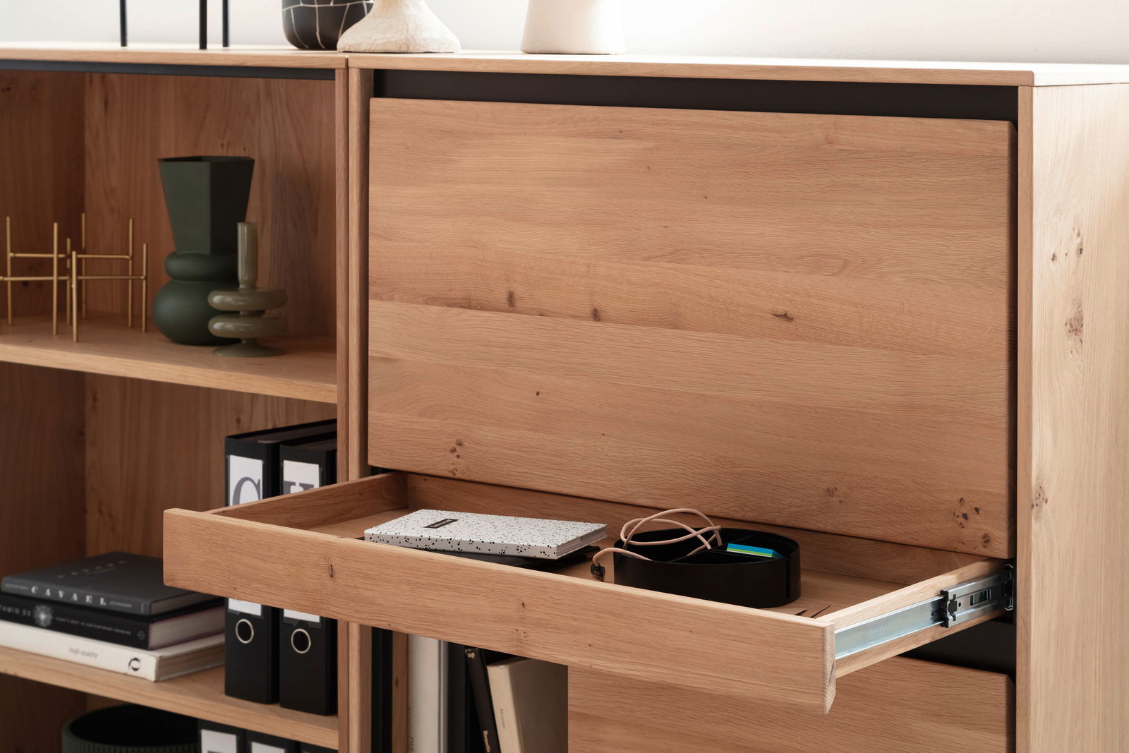 Nahaufnahme eines Holzregals mit Schublade, die teilweise geöffnet ist. Sichtbar sind Bücher, Ordner und Dekorationsgegenstände. Perspektive von vorne.