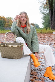 Carrybag Rhombus Olive in einer herbstlichen Umgebung, von vorne fotografiert, neben einer Person mit olivgrüner Jacke und orangefarbenen Stiefeln.