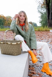 Carrybag Rhombus Olive in een herfstachtige omgeving, van voren gefotografeerd, naast een persoon met een olijfgroen jasje en oranje laarzen.
