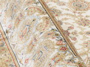 Nahaufnahme eines Orientteppichs mit floralen Mustern in Beige, Rot und Blau, perspektivisch von der Seite aufgenommen.