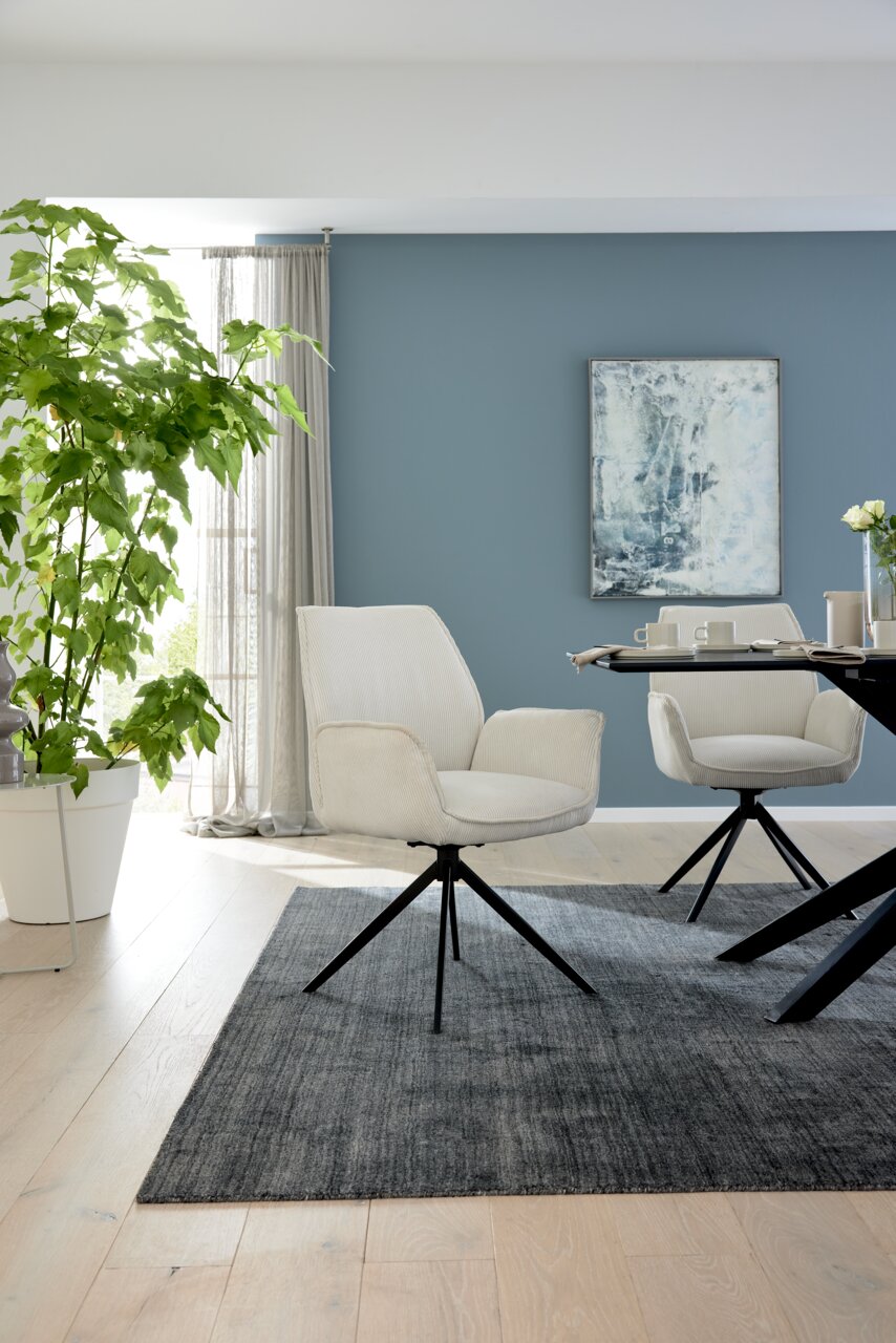 Moderner Armlehnstuhl in hellem Stoffbezug mit schwarzem Metallgestell, seitliche Perspektive im stilvollen Wohnraum.