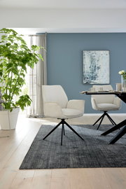 Moderner Armlehnstuhl in hellem Stoffbezug mit schwarzem Metallgestell, seitliche Perspektive im stilvollen Wohnraum.