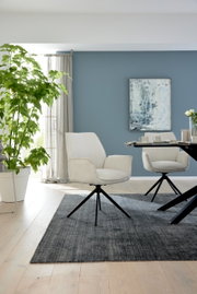Moderne fauteuil met lichte stoffen bekleding en een zwart metalen frame, gezien vanaf de zijkant in een stijlvolle woonkamer.