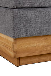 Nahaufnahme eines Boxspringbettes mit grauem Stoffbezug und Holzrahmen, Perspektive von der Ecke