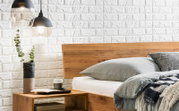 Holzbettgestell mit Kopfteil aus Holz, seitliche Perspektive, dekoriert mit Kissen und Decke, daneben ein Nachttisch mit Vase und Lampe.