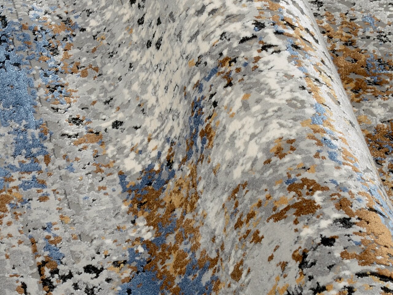 Nahaufnahme eines Designer Teppichs mit abstraktem Muster in Blau-, Grau- und Brauntönen, aus seitlicher Perspektive aufgenommen.