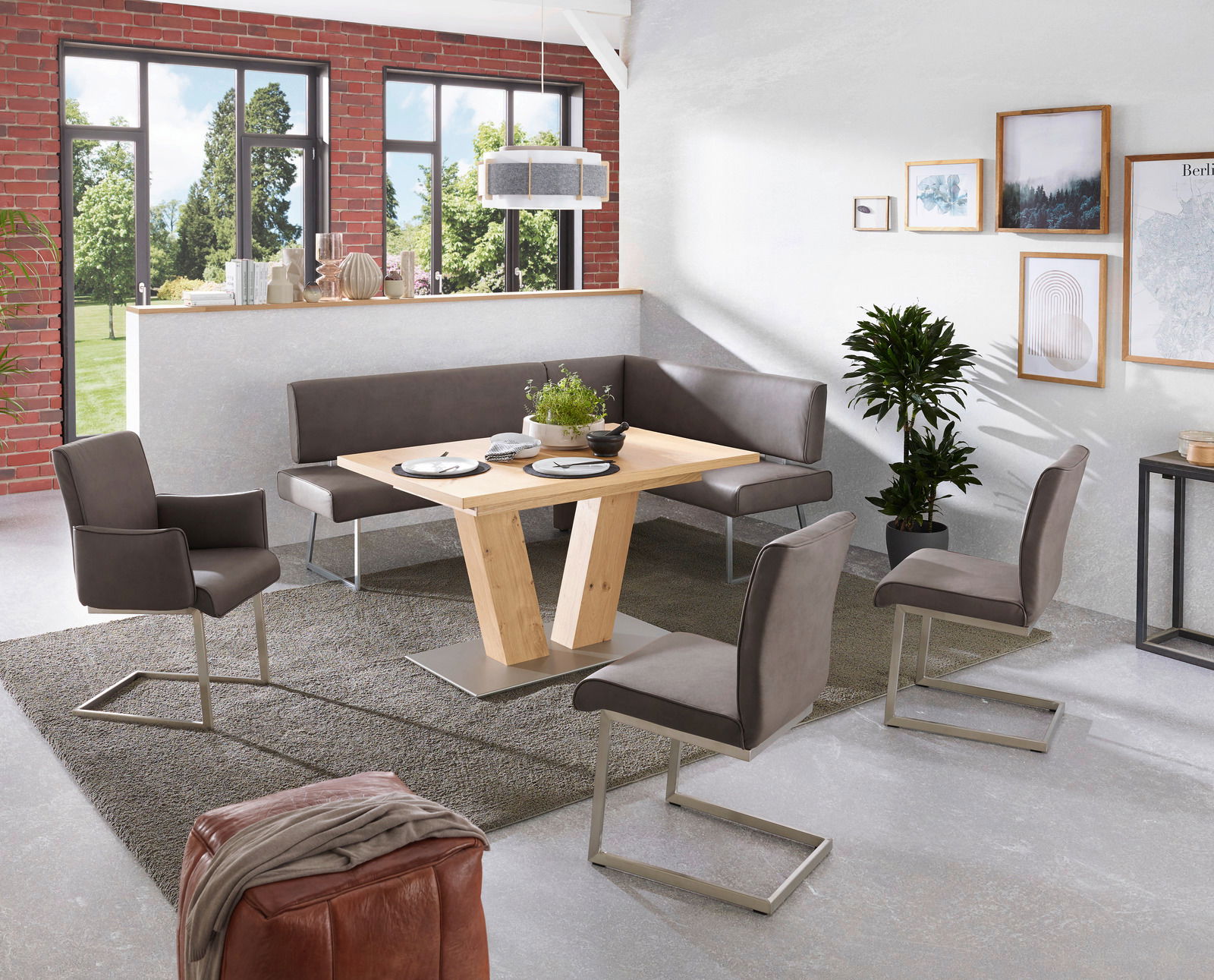 Moderner Esstisch aus Holz mit V-förmigem Gestell, umgeben von grauen Stühlen und einer Eckbank in einem hellen Raum mit großen Fenstern. Perspektive: seitlich von oben.