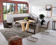 Moderner Esstisch aus Holz mit V-förmigem Gestell, umgeben von grauen Stühlen und einer Eckbank in einem hellen Raum mit großen Fenstern. Perspektive: seitlich von oben.