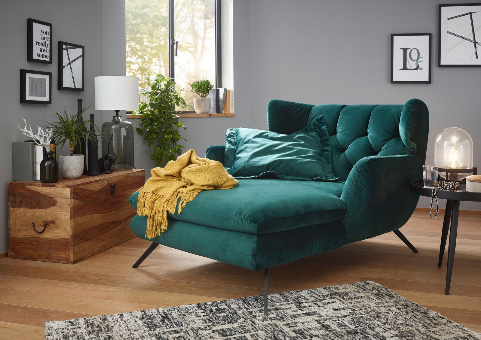 Grünes Longseat mit Samtbezug in einem modernen Wohnzimmer, seitliche Perspektive, dekoriert mit gelber Decke und Kissen.