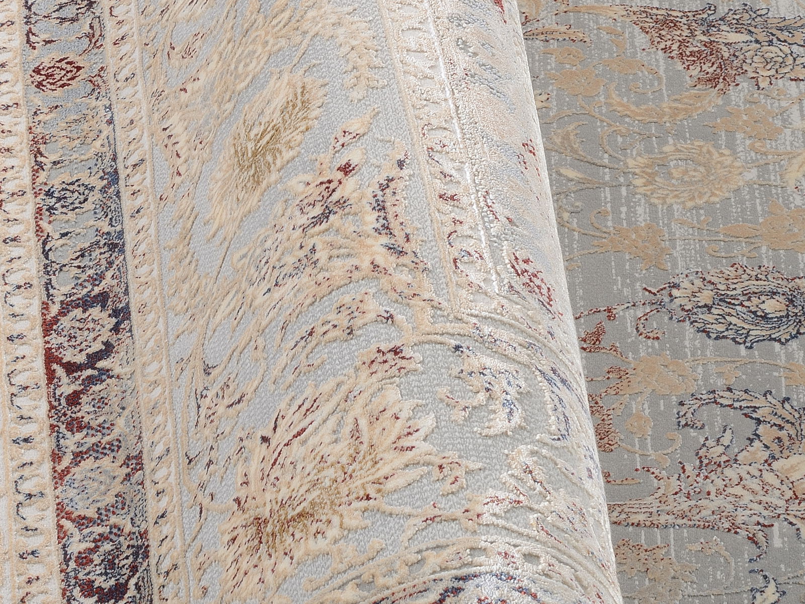 Nahaufnahme eines Orientteppichs mit floralen Mustern in Beige, Blau und Rot, perspektivisch von der Seite aufgenommen.