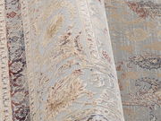 Nahaufnahme eines Orientteppichs mit floralen Mustern in Beige, Blau und Rot, perspektivisch von der Seite aufgenommen.