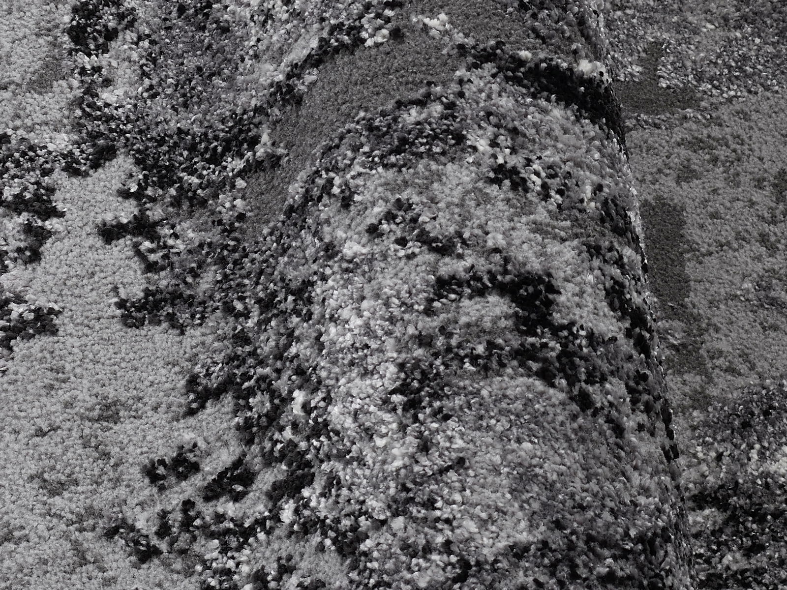 Nahaufnahme eines Designer-Teppichs mit abstraktem Muster in Grautönen, aus seitlicher Perspektive aufgenommen.