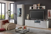 Moderne Wohnzimmeransicht mit einer weißen Vitrine, die von vorne gezeigt wird, neben einem großen Fernseher auf einem weißen TV-Schrank. Ein bequemer Sessel mit Kissen und ein Couchtisch mit Dekorationen runden das stilvolle Ambiente ab.