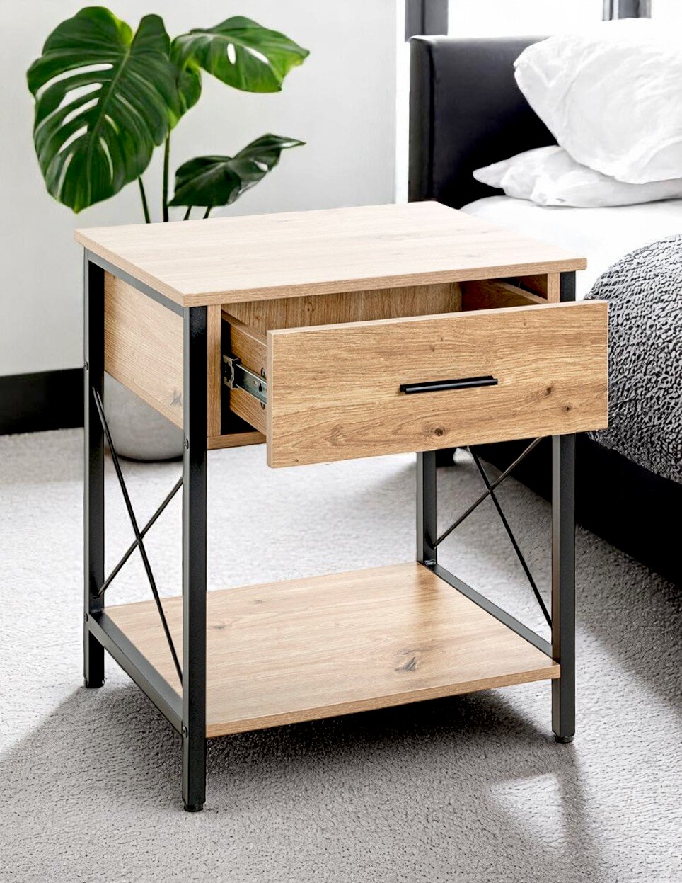 Nachttisch im Industrial-Design aus hellem Holzdekor mit schwarzem Metallrahmen, einer halb geöffneten Schublade und unterer Ablage, seitliche Perspektive im Schlafzimmer neben dem Bett