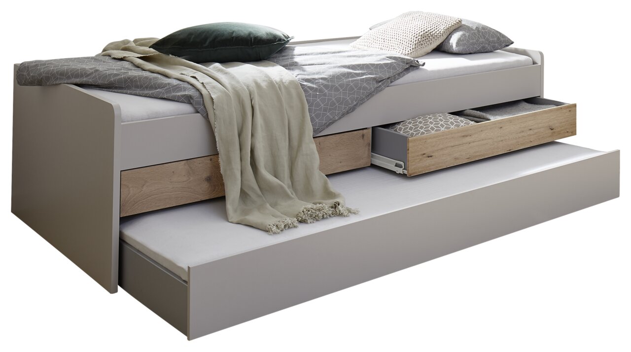 Seitliche Ansicht eines Duo-Liegebetts mit ausziehbarem Bettkasten und Schubladen, dekoriert mit Kissen und Decken.