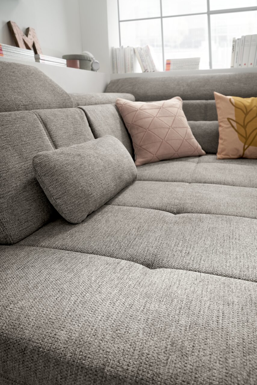 Graue Rundecke mit strukturiertem Stoff, dekoriert mit zwei Kissen in Rosa und Gelb, aus seitlicher Perspektive fotografiert.