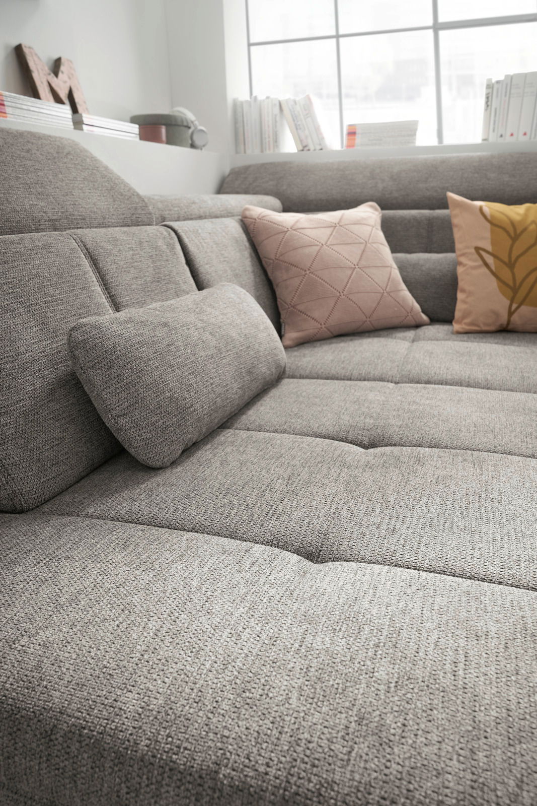 Graue Rundecke mit strukturiertem Stoff, dekoriert mit zwei Kissen in Rosa und Gelb, aus seitlicher Perspektive fotografiert.