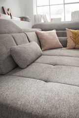 Graue Rundecke mit strukturiertem Stoff, dekoriert mit zwei Kissen in Rosa und Gelb, aus seitlicher Perspektive fotografiert.