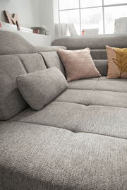 Graue Rundecke mit strukturiertem Stoff, dekoriert mit zwei Kissen in Rosa und Gelb, aus seitlicher Perspektive fotografiert.