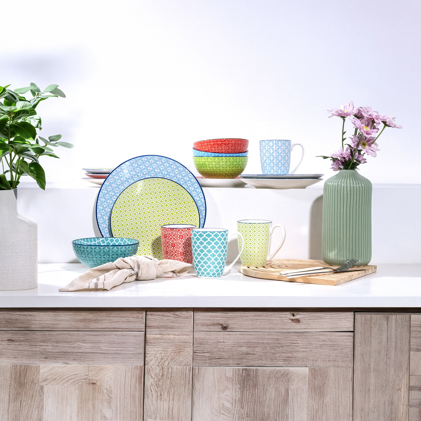 Bunt gemischtes Geschirr mit Tassen, Schalen und Vase auf heller Küchenanrichte.