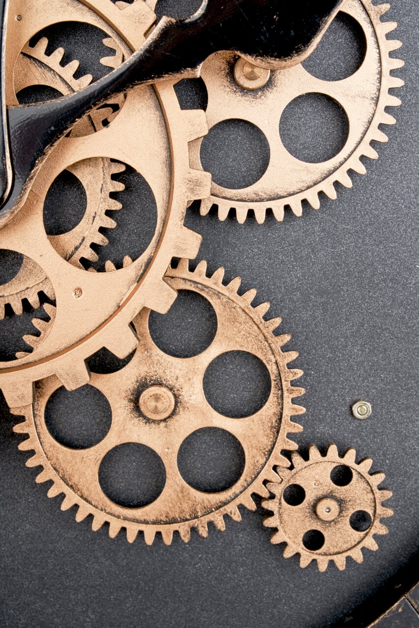 Nahaufnahme einer Wanduhr mit sichtbaren Zahnrädern in einem industriellen Design.