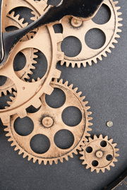 Nahaufnahme einer Wanduhr mit sichtbaren Zahnrädern in einem industriellen Design.