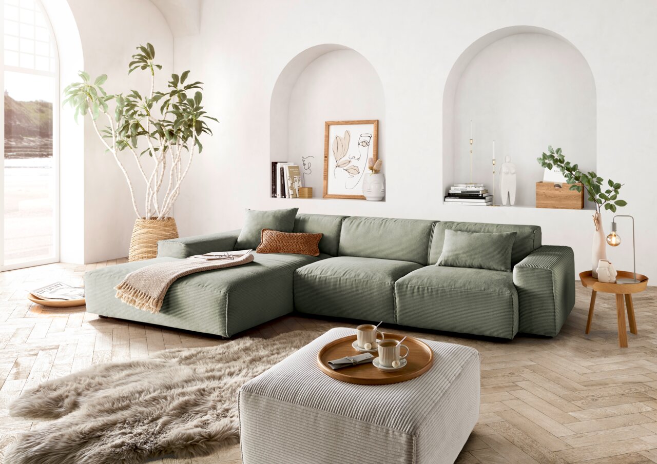 Grünes Ecksofa in modernem Wohnzimmer mit großen Fenstern, Pflanzen und stilvollen Dekorationen, seitliche Perspektive.