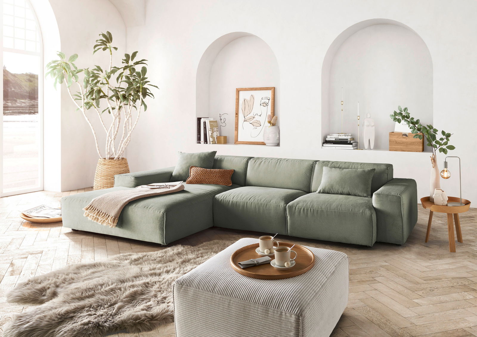 Grünes Ecksofa in modernem Wohnzimmer mit großen Fenstern, Pflanzen und stilvollen Dekorationen, seitliche Perspektive.