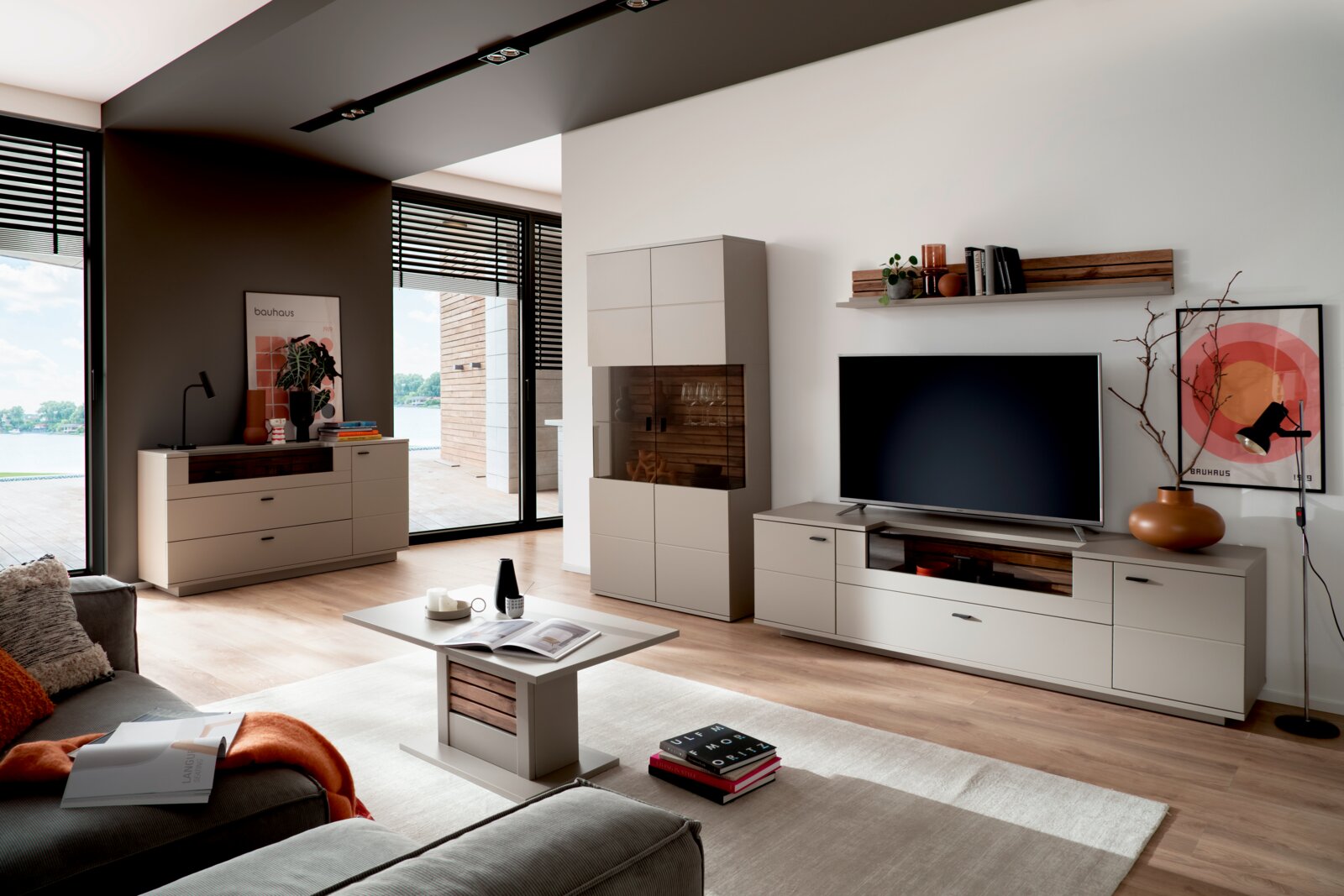 Modernes Wohnzimmer mit hellgrauer Wohnwand (TV-Lowboard und Vitrine) und Couchtisch in Holzoptik, frontale Weitwinkelperspektive leicht von links.
