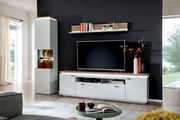 Modernes Wohnzimmer-Entertainment-Set mit weißem TV-Lowboard und passendem Hängeregal in Holzoptik vor dunkler Wand, links hohe Vitrine mit Glasfach; Perspektive: frontale Ansicht mit leichtem Winkel von links.