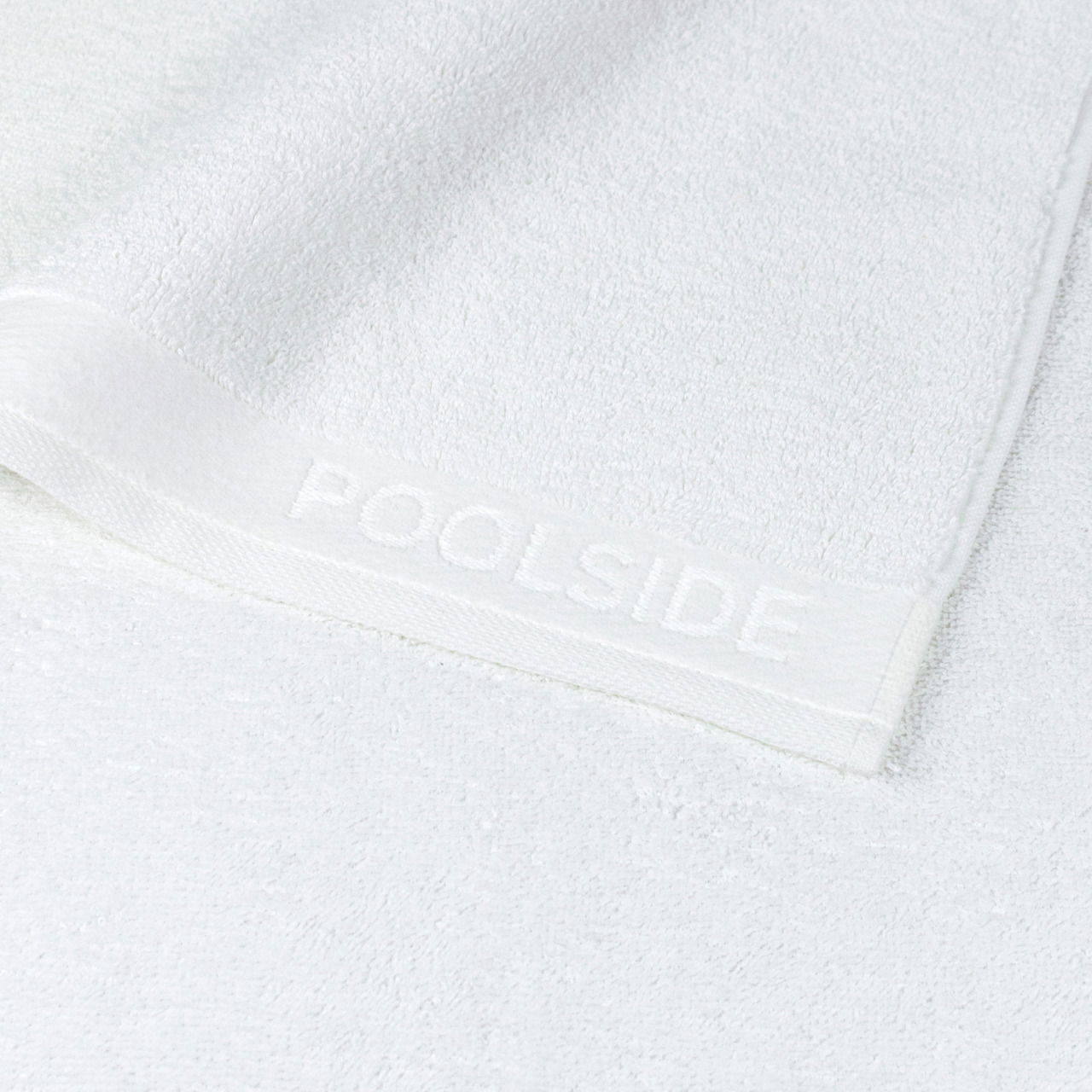 Nahaufnahme eines weißen Handtuchs mit der Aufschrift 'POOLSIDE' auf dem Rand.