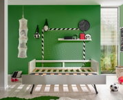 Jugendbett in einem sportlich dekorierten Kinderzimmer mit grün gestrichener Wand, Fußball-Dekorationen und einem großen Fenster. Perspektive: Frontalansicht des Bettes.