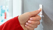 Nahaufnahme einer Hand, die einen tesa Powerstrip Waterproof an einer Wand befestigt. Perspektive von der Seite.
