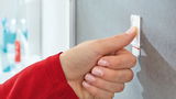 Nahaufnahme einer Hand, die einen tesa Powerstrip Waterproof an einer Wand befestigt. Perspektive von der Seite.