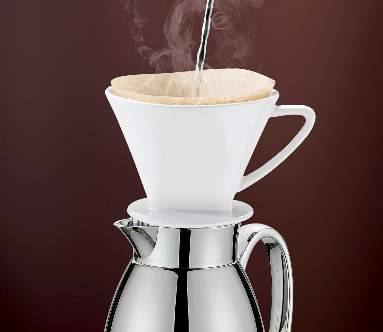 Cilio Isolierkanne Venezia Edelstahl Seitliche Ansicht einer Isolierkanne Venezia aus Edelstahl mit einem weißen Kaffeefilteraufsatz, in den heißes Wasser gegossen wird.
