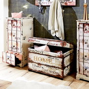 Rustikale Aufbewahrungstruhe aus Holz im Vintage-Shabby-Chic mit Klappdeckel und Schriftzug „HOME“, in seitlicher Perspektive auf dem Boden inszeniert.