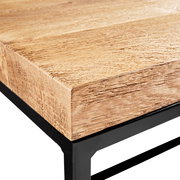 Nahaufnahme eines Couchtischs mit einer robusten Holzplatte und einem schwarzen Metallgestell, Perspektive von der Ecke.