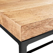 Nahaufnahme eines Couchtischs mit einer robusten Holzplatte und einem schwarzen Metallgestell, Perspektive von der Ecke.