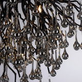 Nahaufnahme einer Deckenleuchte mit tropfenförmigen Glaselementen, die an schwarzen Metallarmen hängen. Die Perspektive zeigt die Leuchte von unten.