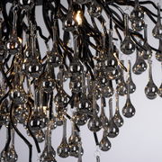 Nahaufnahme einer Deckenleuchte mit tropfenförmigen Glaselementen, die an schwarzen Metallarmen hängen. Die Perspektive zeigt die Leuchte von unten.