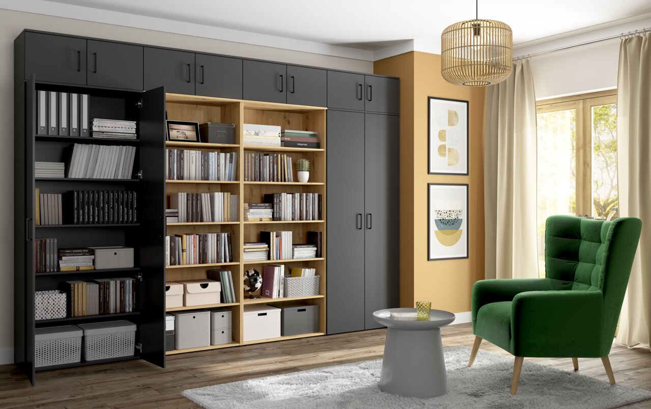 Moderne Wohnzimmeransicht mit einem großen, grauen Mehrzweckschrank und einem offenen Holzregal, gefüllt mit Büchern und Aufbewahrungsboxen. Ein grüner Sessel und ein kleiner runder Tisch stehen vor einem großen Fenster mit Vorhängen. Perspektive: Frontal